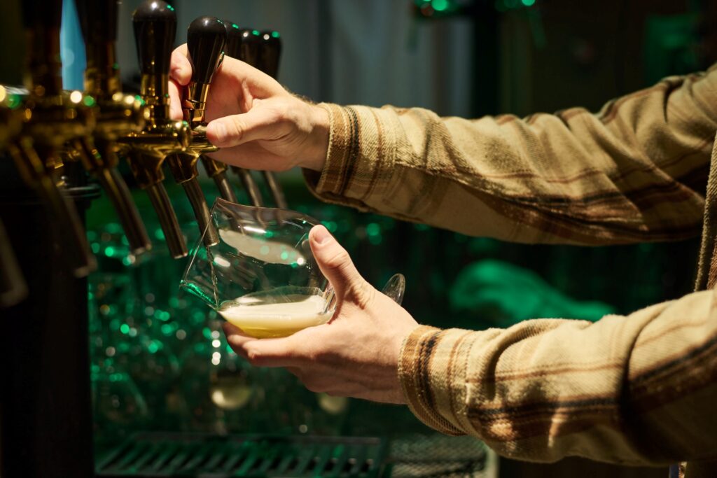 Hand holding a glass angled as beer pours smoothly from a keg tap with minimal foam.