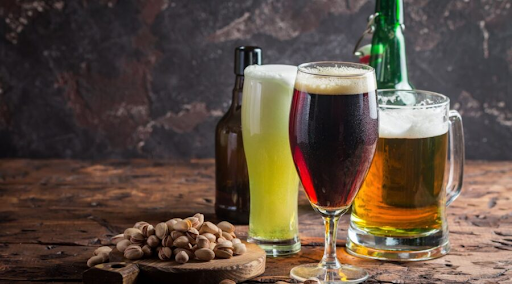 A selection of craft beers in various glasses, with pistachios on a wooden surface.