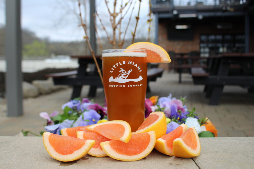Glass of Grapefruit Peace Frog IPA surrounded by fresh grapefruit slices and colorful flowers.
