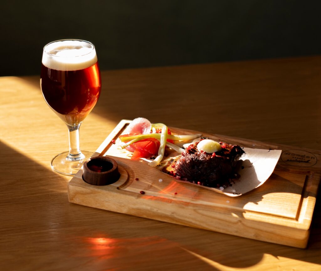 Earthcookie Brown Ale paired with grilled steak, fermented vegetables, and buttered bread on a rustic cutting board.