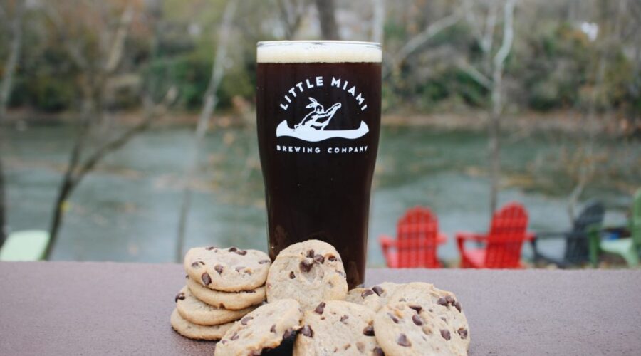 A glass of Little Miami Brewing Company’s Earthcookie Beer Nut Brown Ale set against a scenic background.