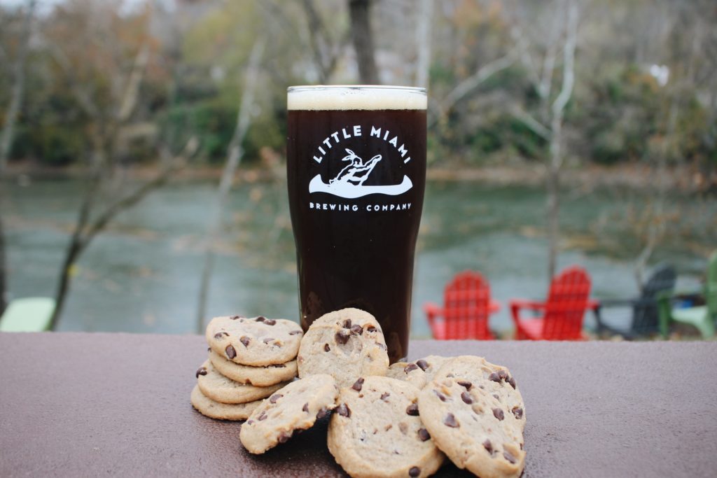 LMBC’s Earth Cookie Brown Ale poured next to chocolate chip cookies on a textured surface.