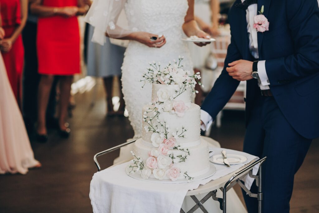 three-tiered wedding cake decorated with pink and white roses A three-tiered wedding cake decorated with pink and white roses, topped with baby's breath, as the bride and groom prepare to serve.