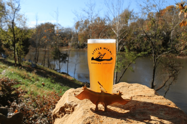 A pint glass filled with golden beer A pint glass filled with golden beer sits on a rock overlooking a scenic river.