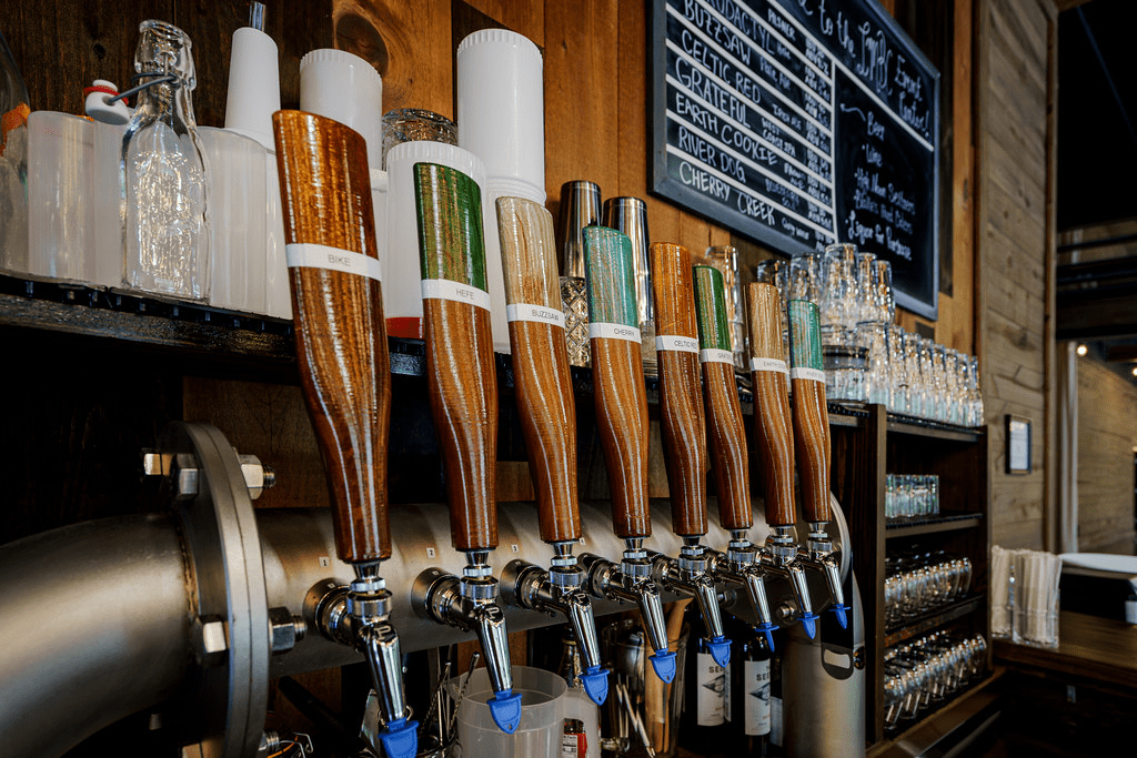 A close-up of a bar with several beer taps A close-up of a bar with several beer taps, each with a different colored handle and a variety of beer glasses lined up on the shelf.