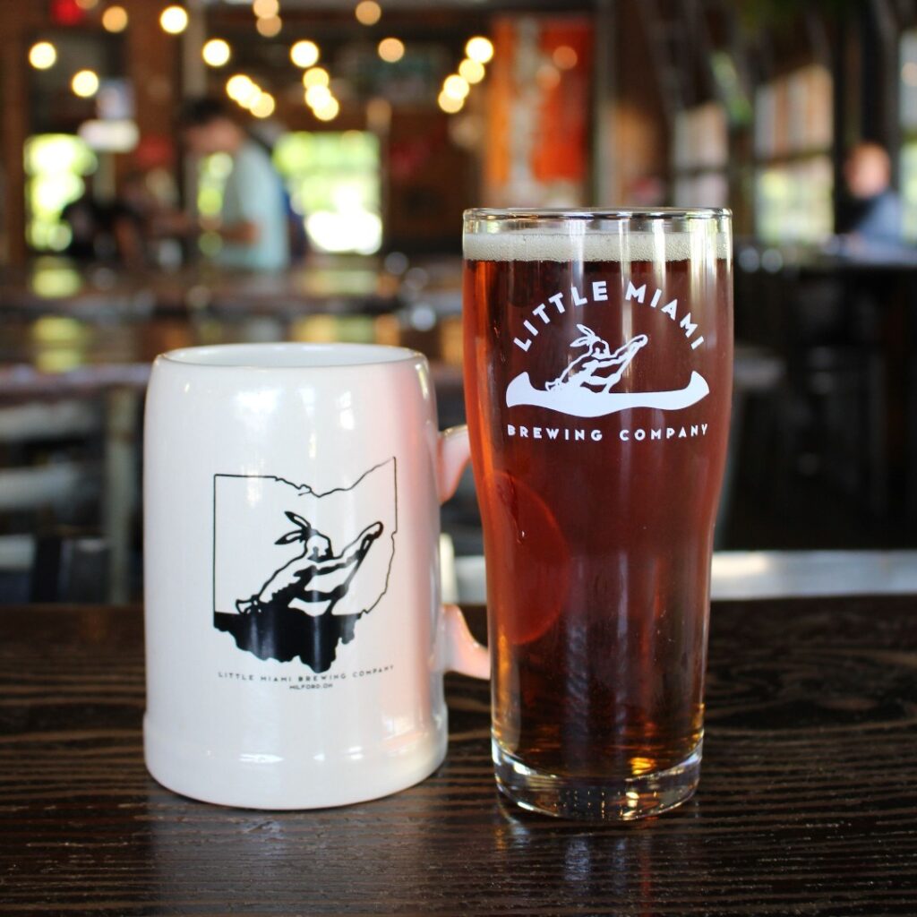 Pilsner Urquell Beer Little Miami Beer and a ceramic mug on a dark wooden table.