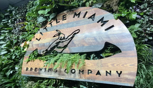 Wooden sign of Little Miami Brewing Company Wooden sign of Little Miami Brewing Company surrounded by lush greenery, highlighting the natural vibe of this craft beer brewery.
