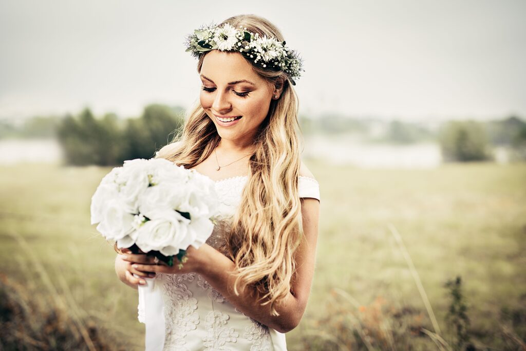 Bride embracing a floral rustic wedding theme Bride embracing a floral rustic wedding theme, holding a white bouquet and wearing a flower crown in an outdoor countryside setting.