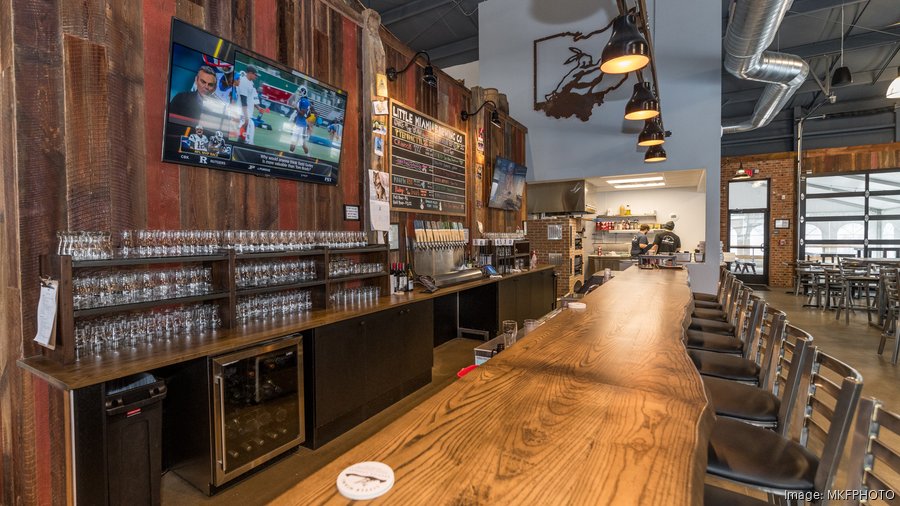 This image captures the inviting atmosphere of a pub This image captures the inviting atmosphere of a pub. A tall glass of beer with a foamy head rests on a wooden bar counter, illuminated by warm lighting. The background is blurred, suggesting a lively and bustling environment.