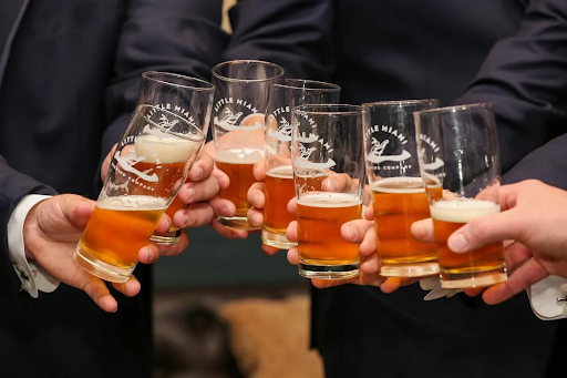 A group of six people in suits toasting with glasses of amber beer from Little Miami Brewing Company, celebrating together.