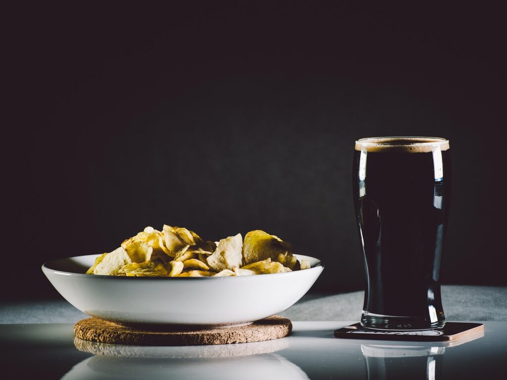 Shot of a glass of beer and potato chips as a snack on the side.