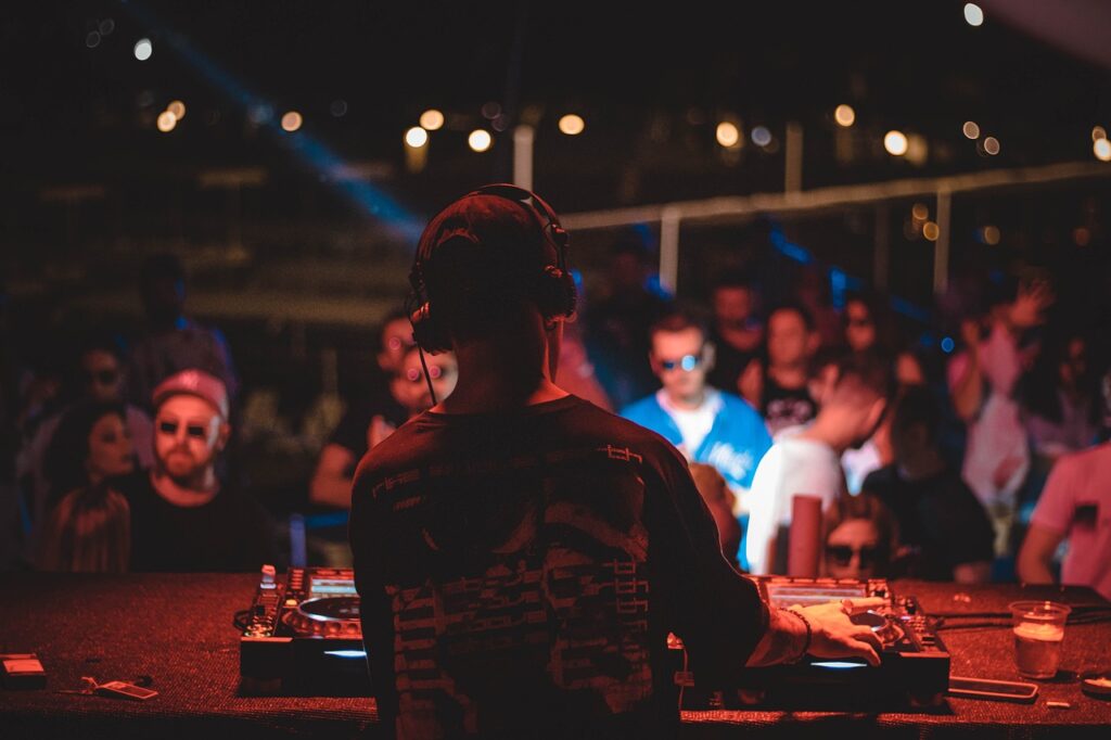 A DJ wearing headphones and a black shirt mixing music, with an audience in the background under vibrant lights.